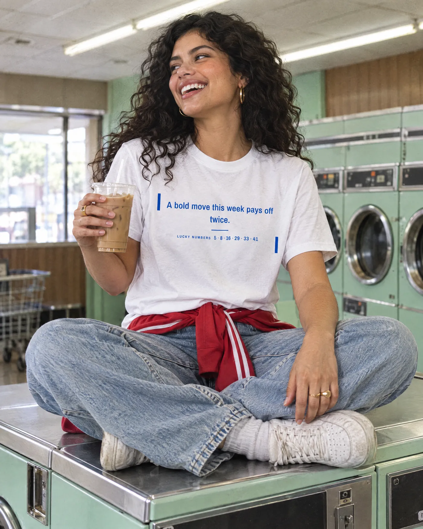 Woman laughing on a washing machine in a retro laundromat, wearing the Fortune Cookie Shirt