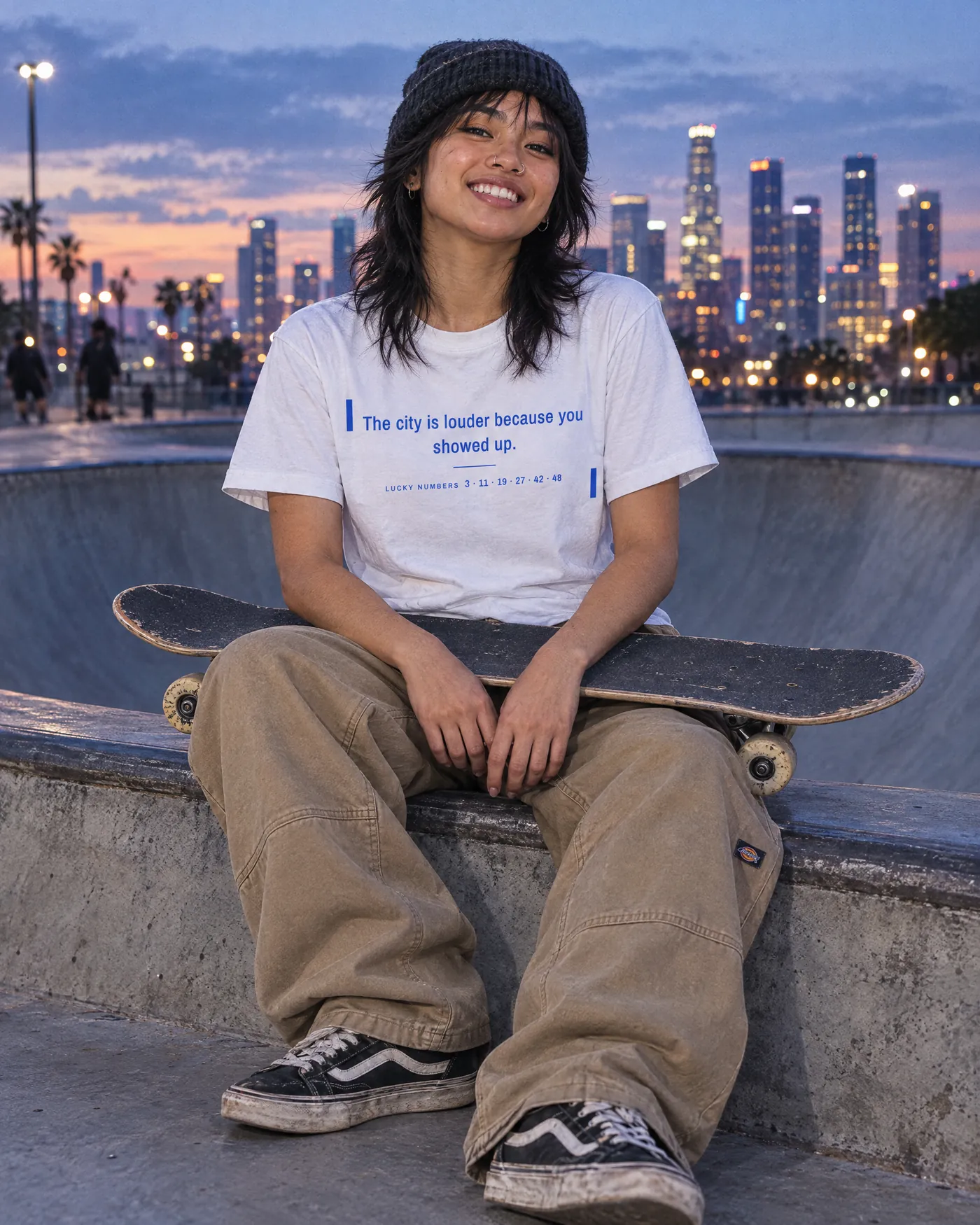 Skater in the Fortune Cookie Shirt sitting on a bowl at dusk with the city skyline behind